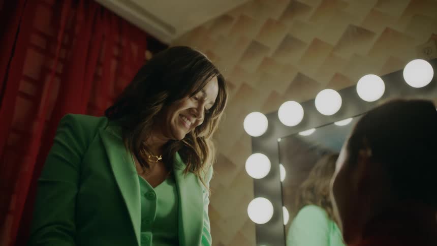 A woman in a green jacket speaks to a person seated in front of them