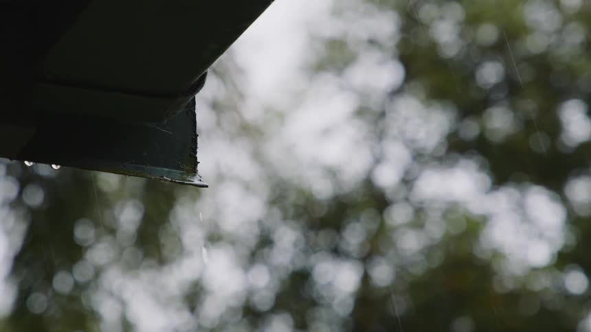 Close up of water dripping from the roof of a house near the trees at daytime