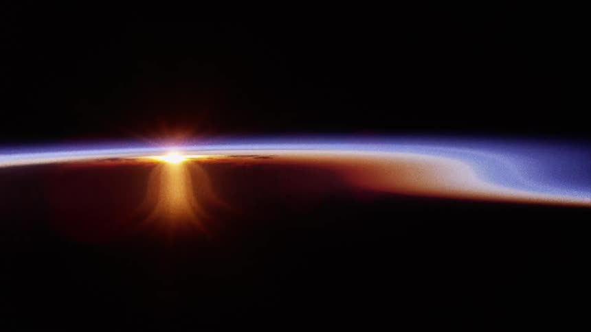 An aerial of sunlight shining over a black horizon