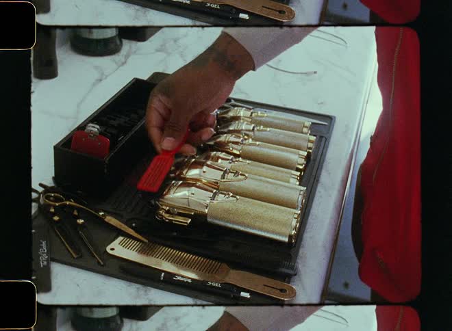 A man is standing over gold plated barber tools and using a small brush to clean them
