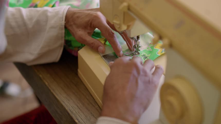 Close up of an elderly mans hands while sewing a dress at a sewing machine