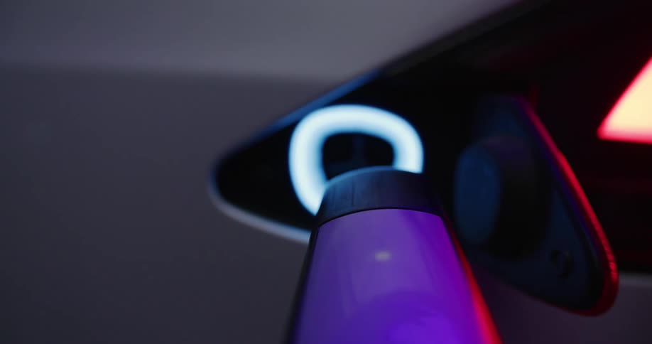 Point of view of a charging cable as it's connected to the charging port of electric car at night