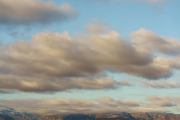 Sunlight shines on cumulus clouds as they float over mountains as they move across the sky