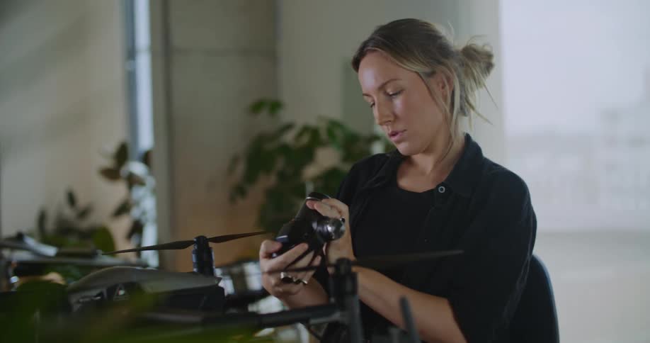 Woman examines camera while sitting in office at desk with drone