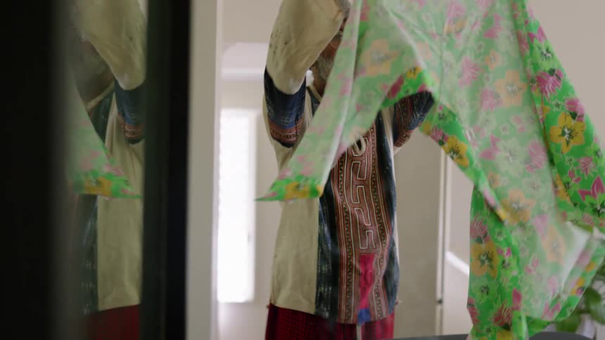 An elderly man is ironing some clothes in the day time