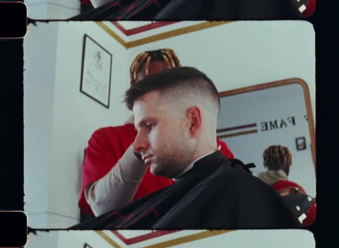 An employee is giving the customer a hair cut at the barber shop