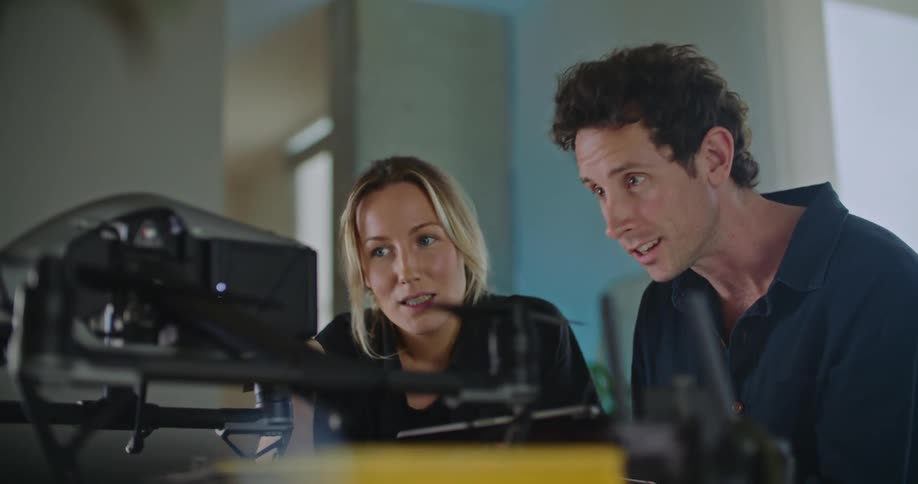 Two people on a room talk while configuring a drone over a table