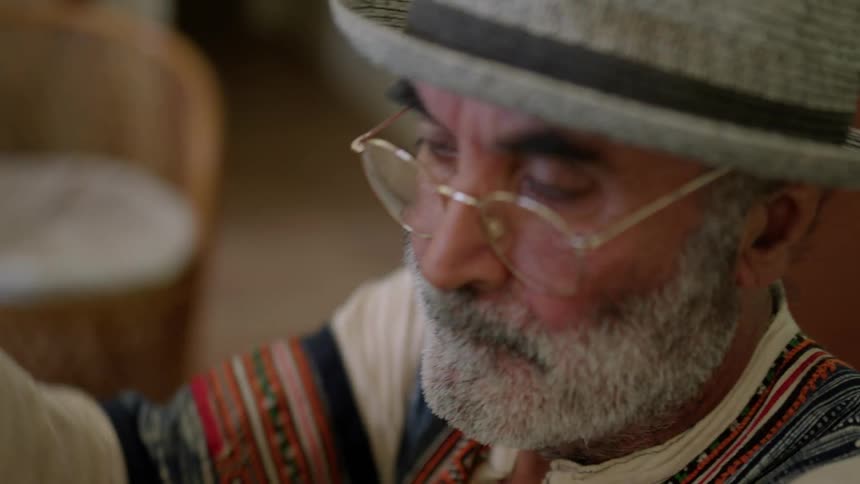 An older elderly man is sitting down inside of his home
