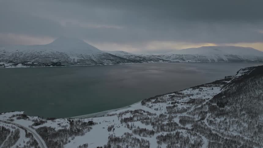 Aerial view of mountains covered in snow close to a river on an overcast day