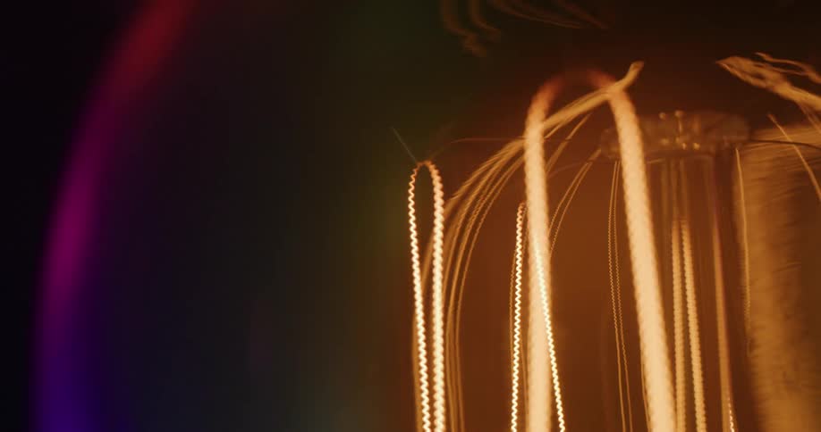 An extreme close up of a light bulb as the light turns on and reflects colored light off the bulb