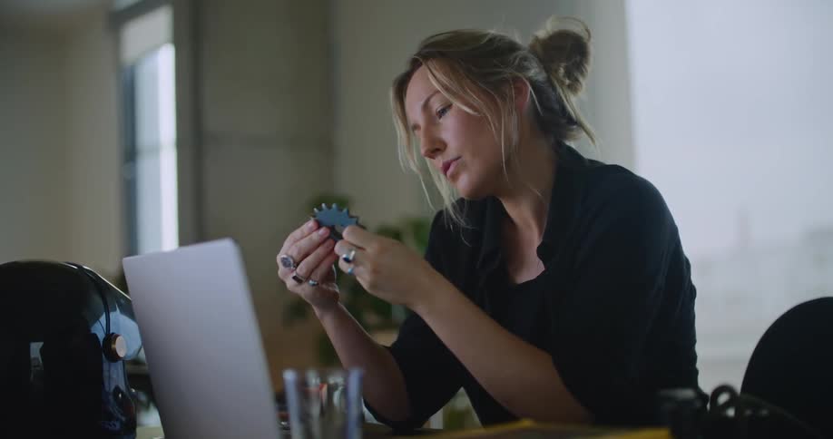 A woman sitting at her desk in front of her laptop looking at a spiral part in her hand