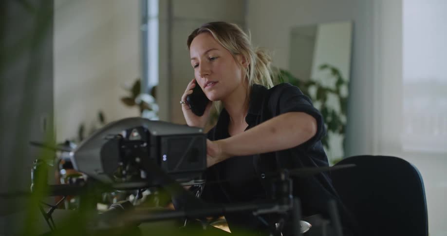 Blonde woman with black shirt talks on smartphone checking drone camera