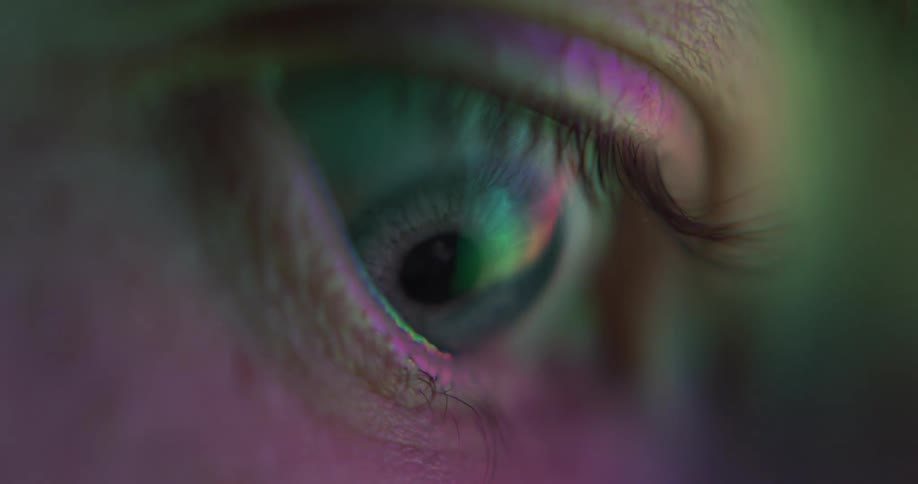 Close up of the blue eye of a woman under changing colorful lights