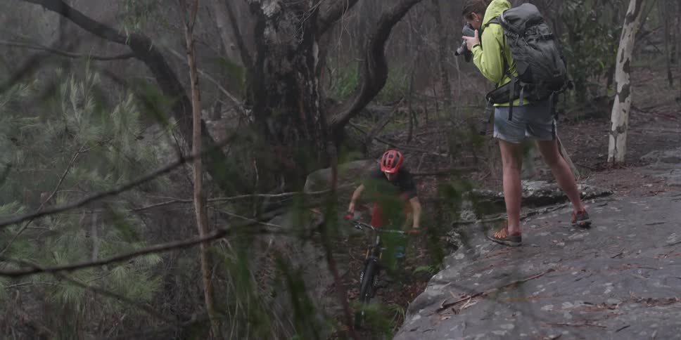 A man is taking photographs as a mountain biker rides downhill