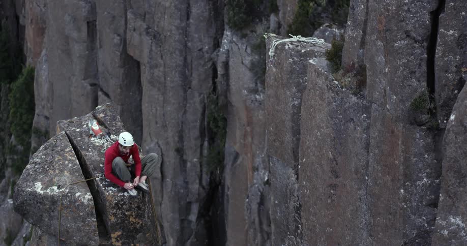 A rock climber sits atop a narrow rock pedestal