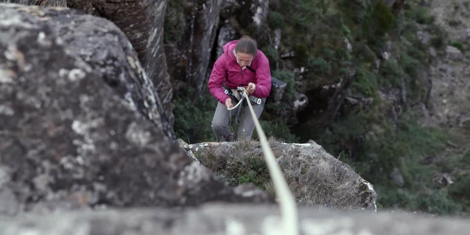 A woman climbing up the side of a steep cliff
