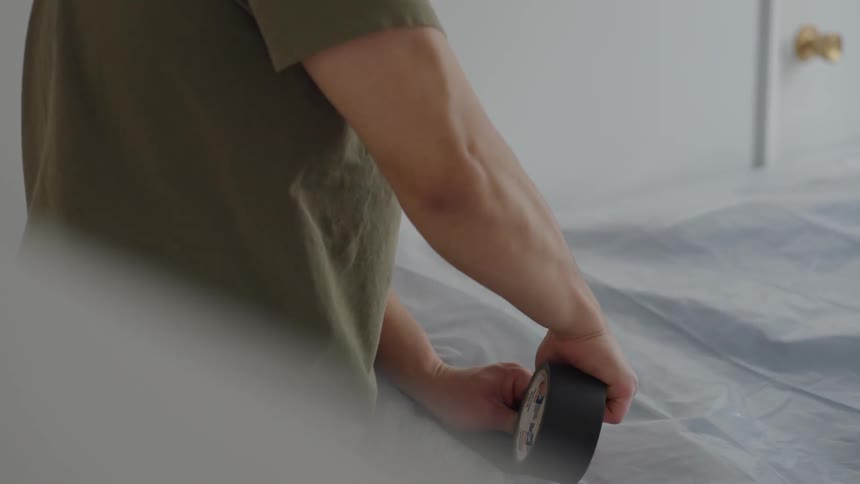 A man uses heavy duty tape to tape a tarp over a large object
