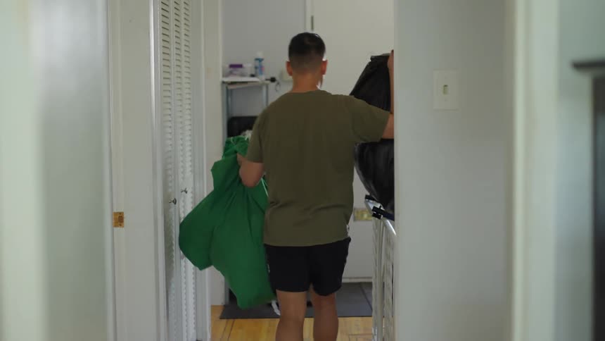 A man carries full trash bags through his house