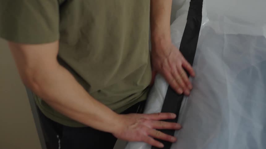 A man folding clothes in a white bag looking behind him