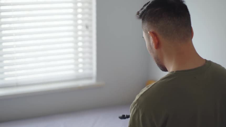 A man is standing in a bedroom wrapping up an electrical cord in his hands