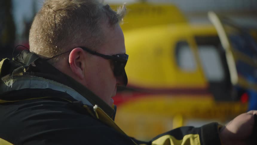 A man puts on a beanie while sitting outside a helicopter