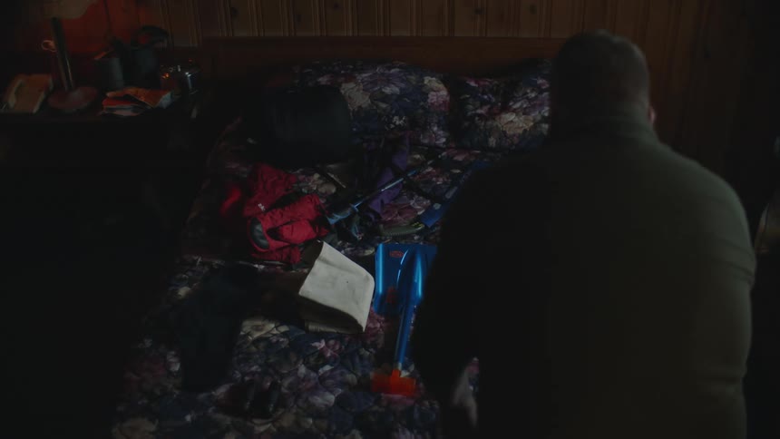 Man leans over camping supplies laid on bed in hotel room