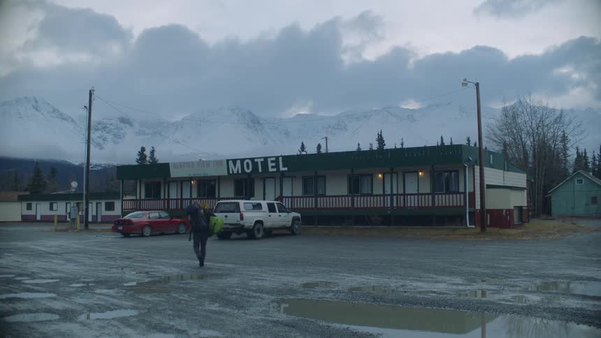 Hiker crosses parking lot toward motel with snow covered mountains in the background