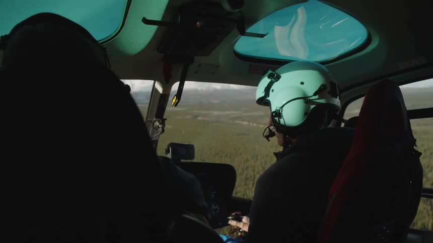 A pilot flies a helicopter over a forest during the day
