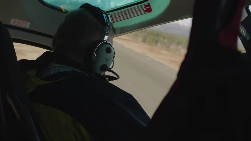 Close up of a pilot flying a helicopter over a forest at daytime