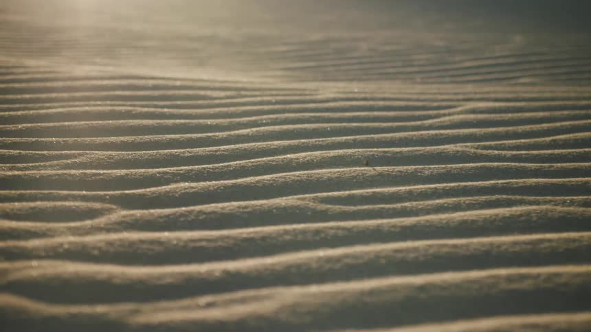 The sun shines brightly upon ripples and wave patterns in the desert sand