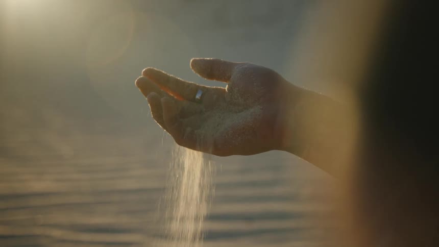 A man on the the desert letting a handful of sand fall through his fingers at sunset