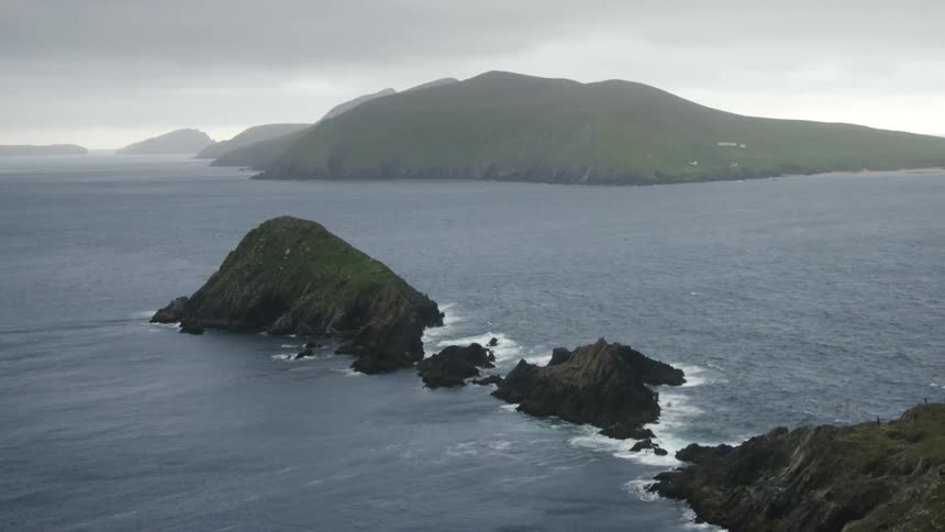 Aerial view of a chain of rocky oceanic islands and ocean waves crashing on their rocky shores on a cloudy day