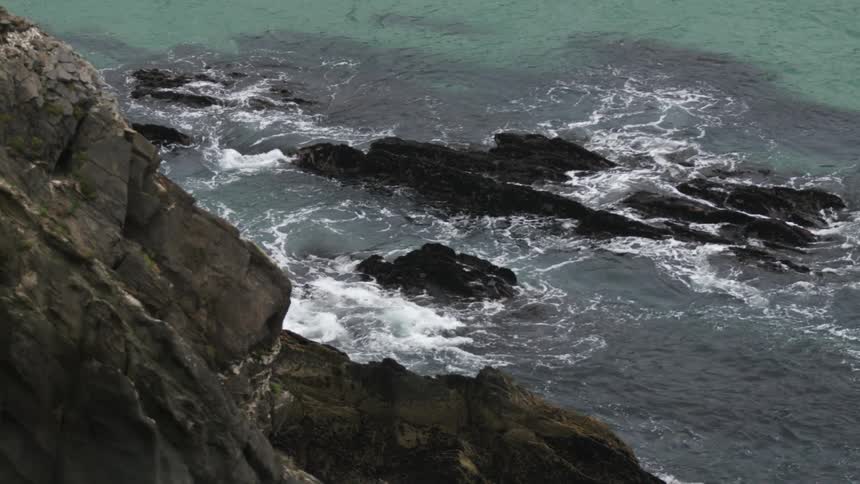 Waves foam while crashing into rocks near seaside cliff
