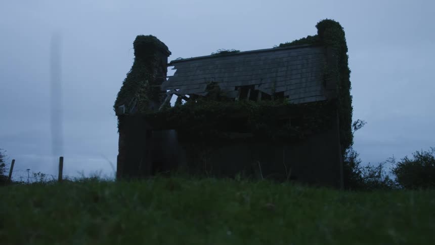 Silhouette of a ruined house on a grass hill in the countryside at evening