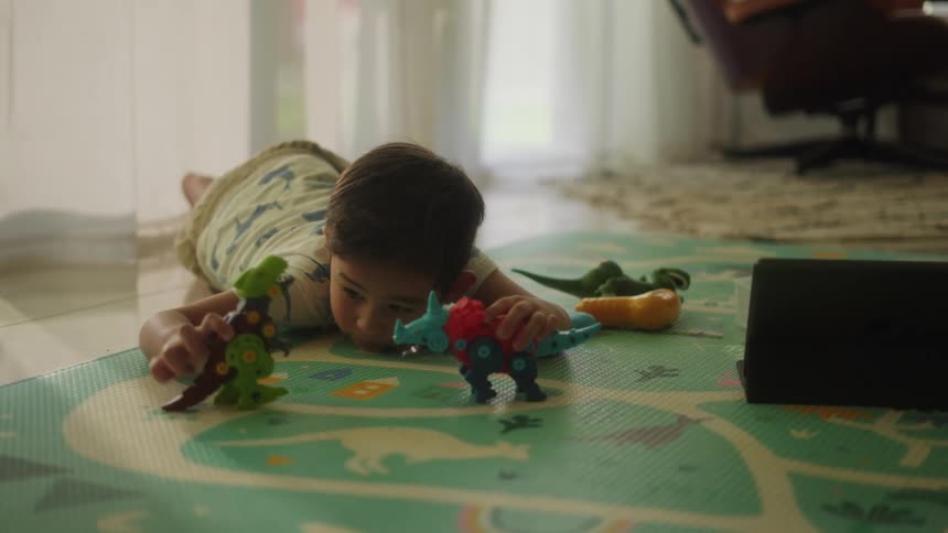A young boy playing with toy dinosaurs on a green mat on the floor