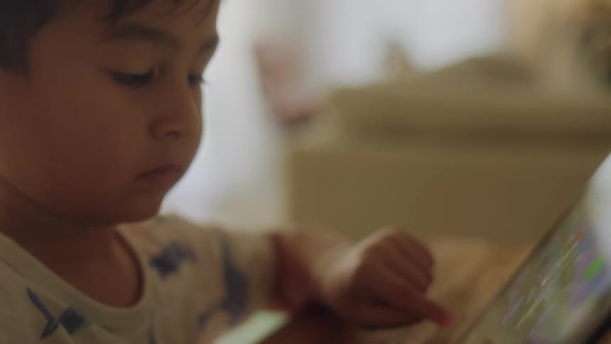 Close up of a boy playing a video game on a tablet in the living room at home