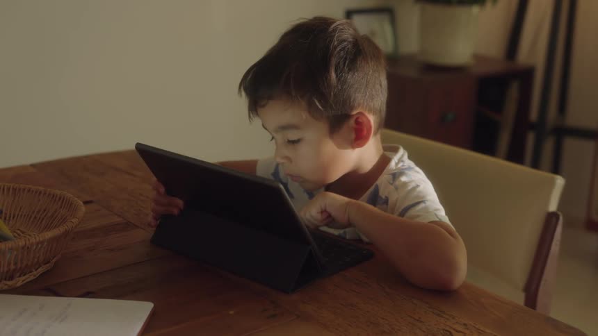 Boy with shirt sits at table using tablet in the living room at home
