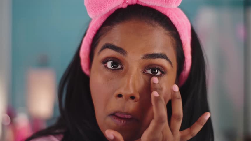A woman uses her fingers to apply makeup to her face