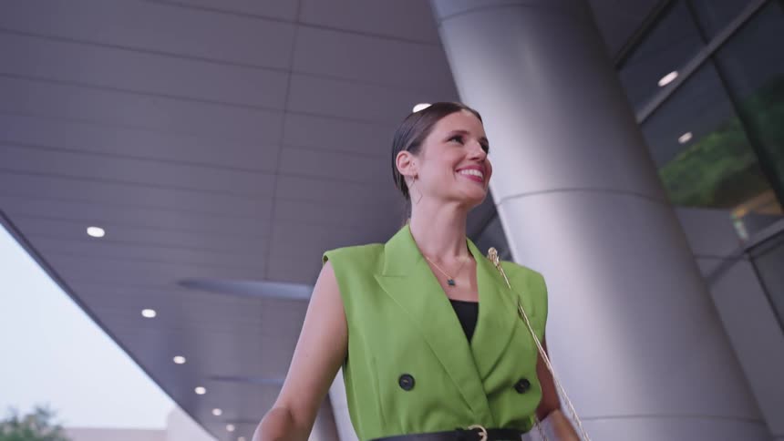 A woman models a trendy green outfit and purse while happily walking near a large building