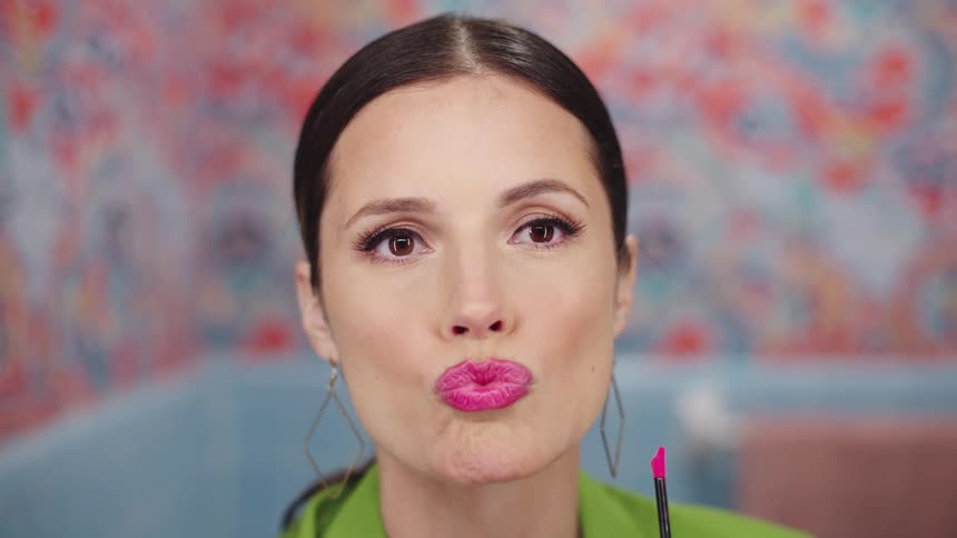 A woman putting on pink lipstick pursing her lips and smiling