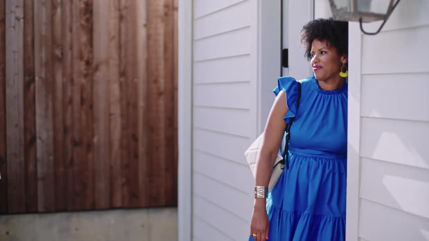 Woman with hoop earrings handbags and curly hair opens door and gets out of house laughing
