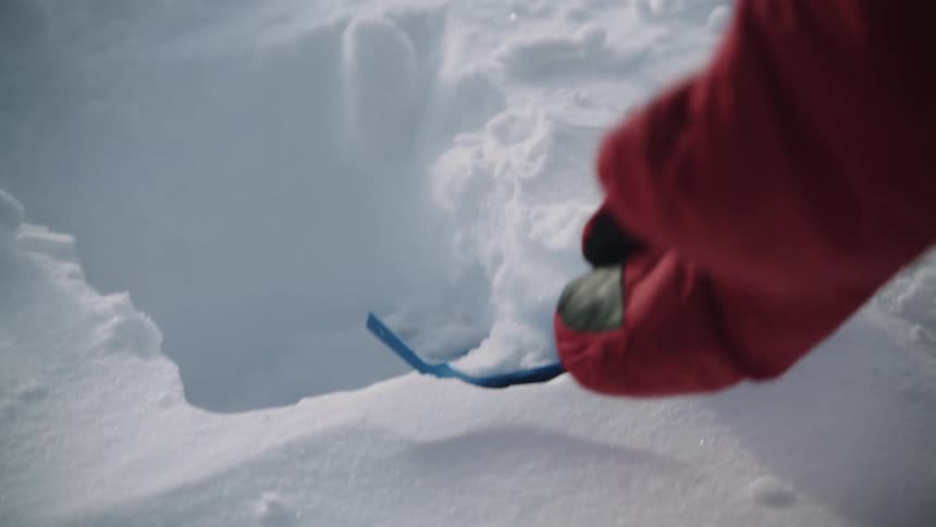A person digs in the snow with a small shovel