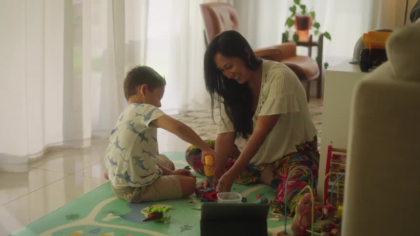 A boy plays with toy tools on the floor with his mom