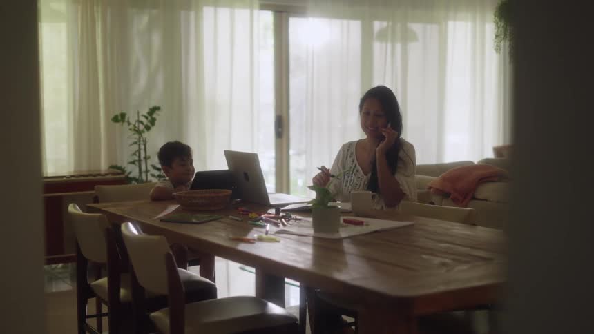 A boy uses a tablet while his mom talks on the phone