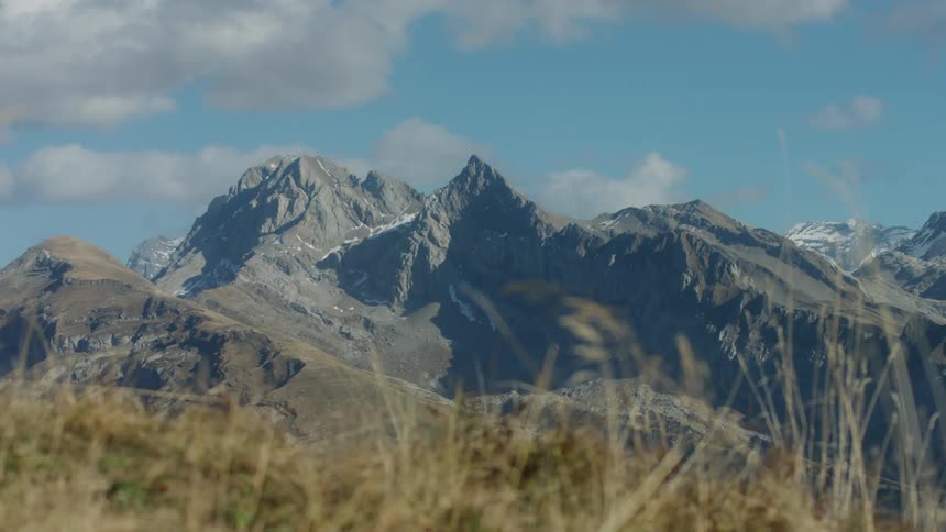 A large mountain peak in the distance and grass up close as a person on a bike rides by quickly