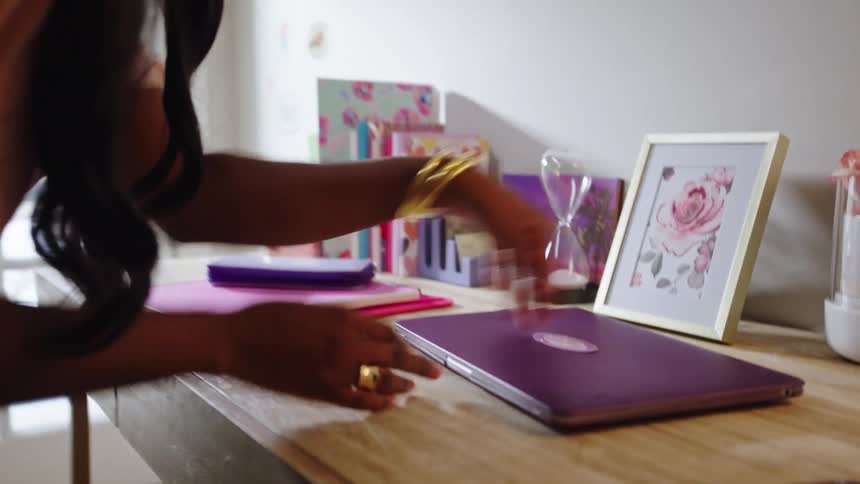 Young woman picks up a laptop from a small desk on her room