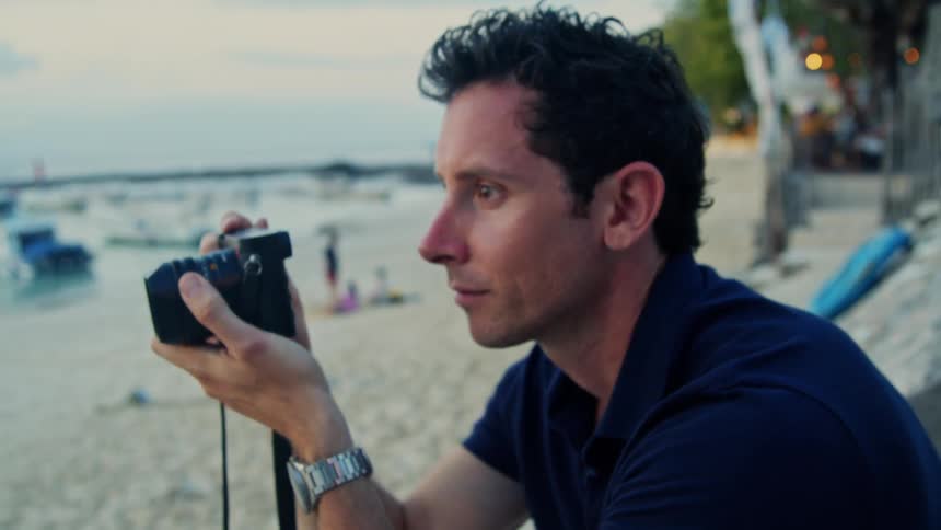 Man in dark blue shirt takes photo with camera on the beach