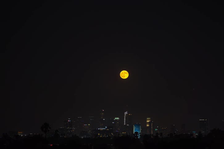 Time lapse of full moon rising over tower blocks in the city at night