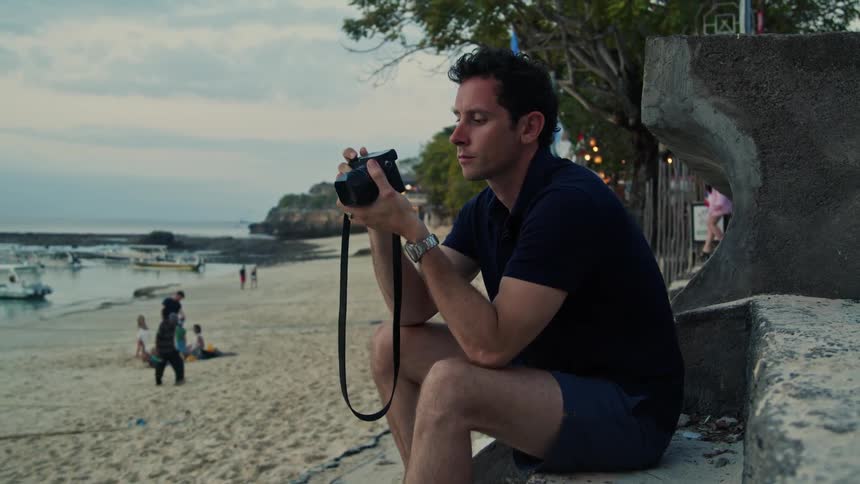 A man is sitting at the beach and taking pictures with a camera