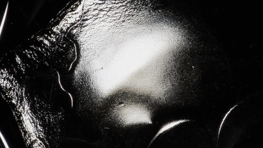 Deep black thick reflective liquid moves slowly in waves and ripples